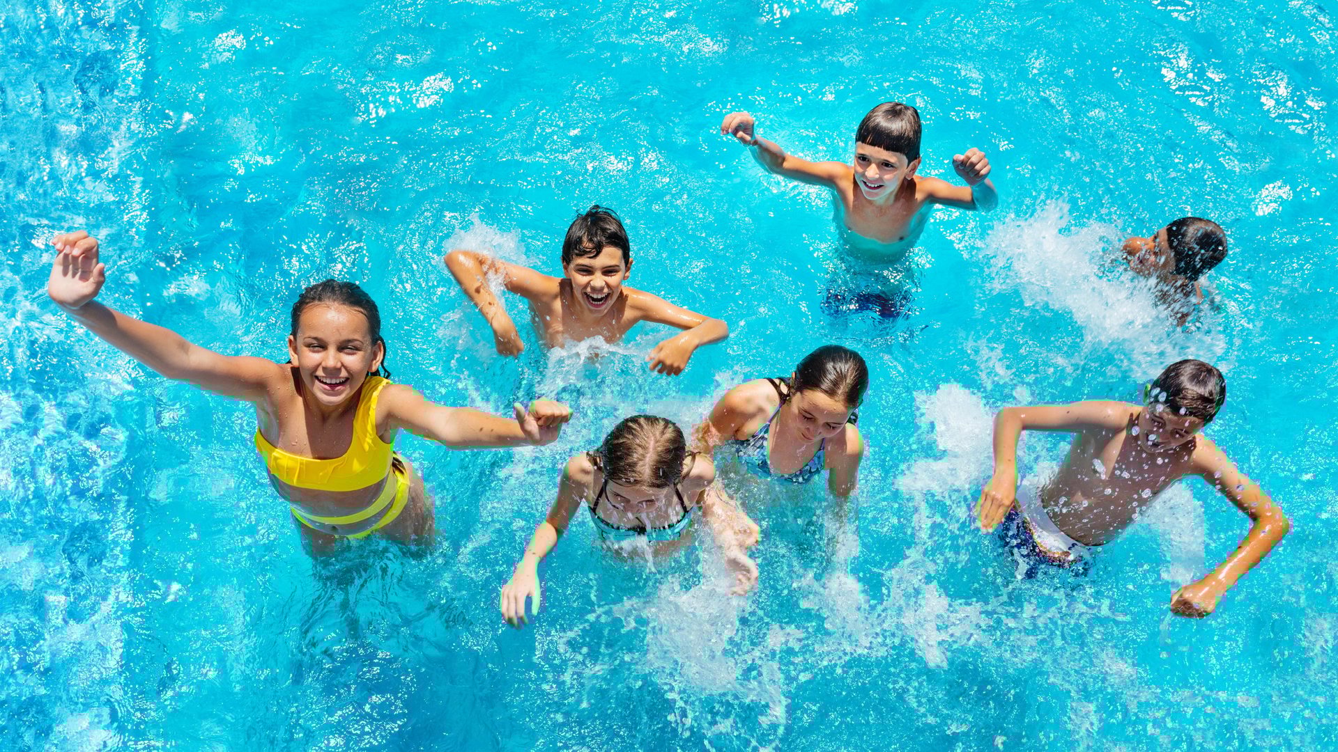 Group of diverse children playing and swimming together in a bright blue swimming pool